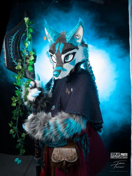 Cosplay anthropomorphe loup bleu-gris, capeline sombre et hache feuillagée — Fabrice Fiorucci Photographe