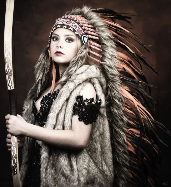 Cosplay amérindienne, coiffe à plumes orangées, fourrure et arc, regard clair — Fabrice Fiorucci Photographe