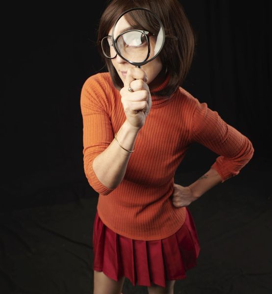 Cosplay Velma Dinkley (Scooby-Doo), pull orange, jupe rouge plissée et loupe en main — Fabrice Fiorucci Photographe
